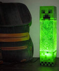Glitter Creeper Mood Light 12 Inch LED Lamp for Gaming Rooms and Kids Rooms Minecraft Themed Neon Glitter Night Light Battery or USB Powered with 15 Minute Auto Shutoff Fun Desk Decor and Glow Gift next to a backpack
