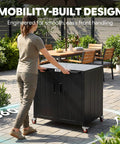 Person pushing Patio-Ready Outdoor Grill Cart With Storage Cabinet And Stainless Steel Top, 35-Inch Grill Station With Door, Modular Kitchen Island For Food Prep And BBQ, Black And Silver on patio