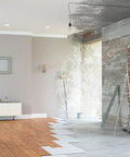 Living room under renovation with visible old brick, drywall, ladder, and partially installed flooring