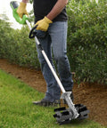 Person using Weed Removal Hand Tool With Tiller Cultivator Wheel Rotary Grass Cutter Attachment for lawn care on grass edge.