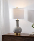 27 Inch Gray And Brass Ceramic Table Lamp For Living Room And Bedroom With White Linen Drum Shade Modern Transitional Nightstand Lamp LED Bulb Included Energy Efficient And ETL Listed on a wooden table.