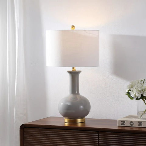 27 Inch Gray And Brass Ceramic Table Lamp For Living Room And Bedroom With White Linen Drum Shade Modern Transitional Nightstand Lamp LED Bulb Included Energy Efficient And ETL Listed on a wooden table.