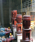Industrial pumps and workers in a concrete facility with large red motors and pipes.