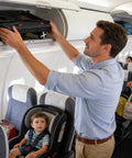 Side view of a man loading a black car-seat travel cart into an airplane overhead bin