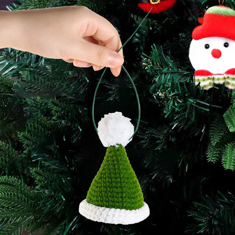 Hand holding green and white knit hat ornament hanging on a Christmas tree