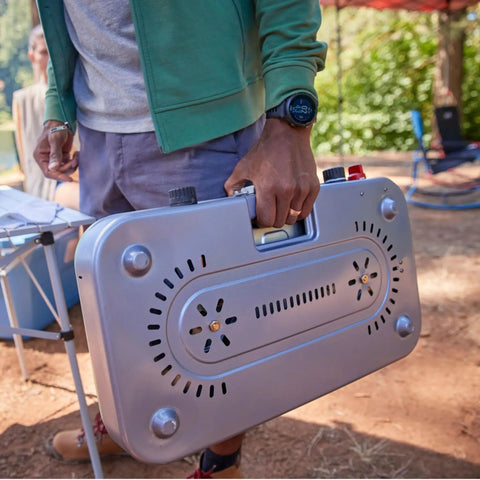Person carrying Three In One Outdoor Camp Stove With Removable Cast Iron Grill And Griddle 24,000 BTUs, showing recessed handle.
