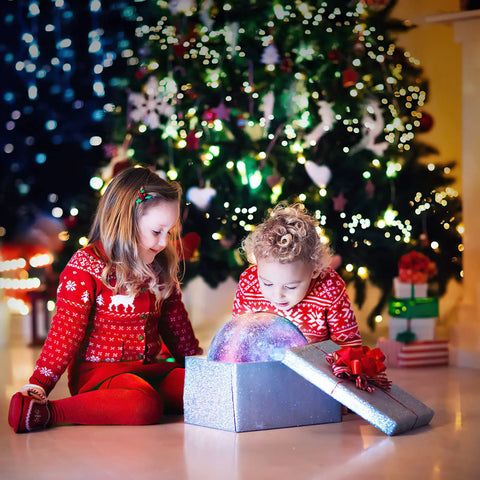 Children in festive sweaters opening gift box with Lit Moon Lamp With Wood Stand Galaxy Night Light In 16 Colors USB Rechargeable Remote And Touch Control 5.9 Inch Safe PLA Material Ideal Gift For Girls And Kids Night Light For Bedroom Decor Perfect Gift For Birthday And Holiday Soft Glow Safe BPA Free