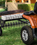40 Inch Tow Behind Spike Aerator For Lawns With 11 Star Shaped Galvanized Plug Core Tines, attached to an ATV on lawn