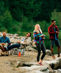People enjoying fishing by a lake with rods and camping gear, surrounded by nature.