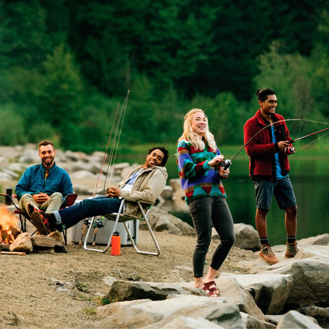 People enjoying fishing by a lake with rods and camping gear, surrounded by nature.