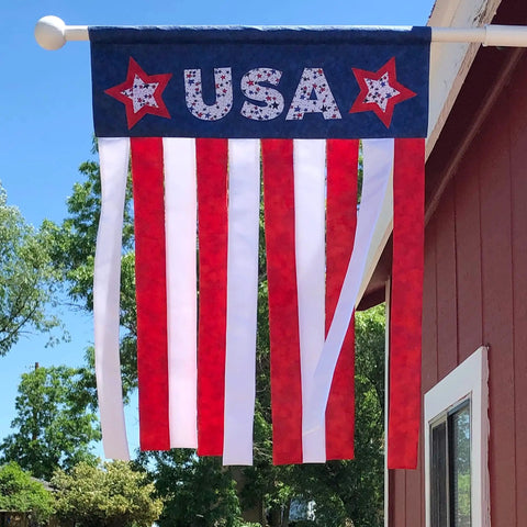 USA banner with red, white, and blue stripes hanging outdoors on a sunny day.
