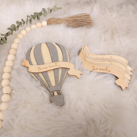 Wooden Hot Air Balloon Monthly Milestone Cards For Babies, My First Year Sign set on fluffy surface with greenery.