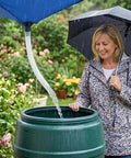 Woman collecting rain in barrel using Rainwater Collection System With Hose, Water Storage Bag And Roof Drain Fitting Tarp For Lawn, Garden.