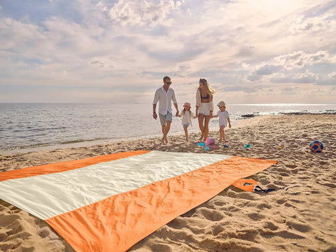 Sandproof And Waterproof Beach Blanket 7x7 Ft Extra Large Mat With Stakes on sand, family in background, sunny beach setting.