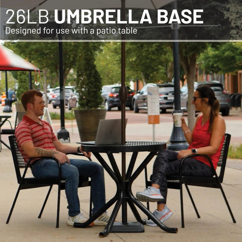 Heavy Duty 26 Pound Cast Stone Outdoor Umbrella Base Stand For Patio Tables Fits Umbrella Poles 1.3 To 1.8 Inches Black Ultra Stable Foundation For Decks And Backyards That Keeps Your Patio Umbrella Solid And In Place. Two people sitting at a patio table with an umbrella.