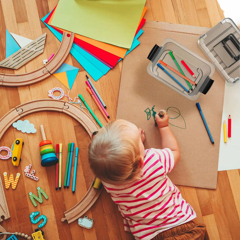 Child drawing on paper with toys and Stackable Plastic Storage Bins Set Clear 6 Quart Nestable Boxes With White Lids nearby.
