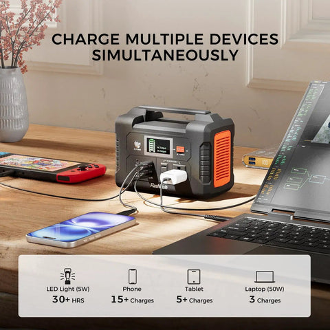 Grab And Go Solar Generator Bundle With Portable Power Station charging multiple devices on a table, including phone and laptop.