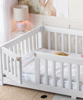 Totally Built Tough Twin Floor Bed With Montessori Design And Complete Safety Guardrails Plus Easy Access Door For Kids, Solid Wood Low Profile Slatted Frame In Fresh White in a bright nursery setting.