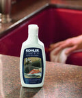 Kohler Cast Iron Cleaner bottle near red cast iron sink, focus on Cast Iron Cleaner For All Cast Iron Surfaces And Cookware Genuine Part Quality Formula
