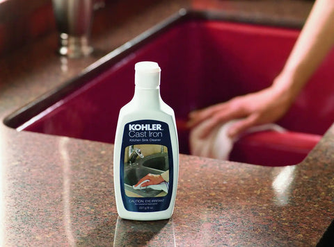 Kohler Cast Iron Cleaner bottle near red cast iron sink, focus on Cast Iron Cleaner For All Cast Iron Surfaces And Cookware Genuine Part Quality Formula