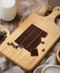 Front view of 11x5 inch bamboo cutting board with handle; chocolate bar pieces arranged on top.
