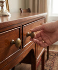 Hand reaching for classic round antique brass cabinet knobs set of 6 with 1 1/4 inch head diameter on wooden drawers.