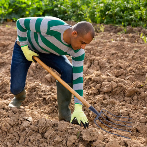 Man using Handheld Manure Fork For Home Gardening And Lawn Cleanup in a field, demonstrating soil preparation.
