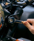 Close-up of hand using a wrench on a motorcycle part, demonstrating tool use from a 152 Piece Basic Household Hand Tool Set.