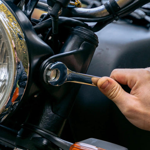 Close-up of hand using a wrench on a motorcycle part, demonstrating tool use from a 152 Piece Basic Household Hand Tool Set.