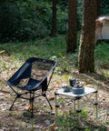 Ultralight Camping Folding Beach Chair With Anti Sinking Large Feet And Back Support Webbing next to table in forest setting