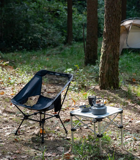 Ultralight Camping Folding Beach Chair With Anti Sinking Large Feet And Back Support Webbing next to table in forest setting
