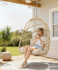 All-Weather Hanging Egg Chair No Stand With 350 Lb Capacity on porch with woman sitting, beige wicker hammock with cushions