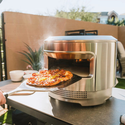 Person using Stainless Pizza Peel With Built In Ridges Serving Board And Pizza Paddle For Ovens 304 Stainless Steel 24 In Long By 11.75 In Wide Lightweight 1.8 Lbs Game Changer For Easy Home Pizza Nights to take pizza from oven