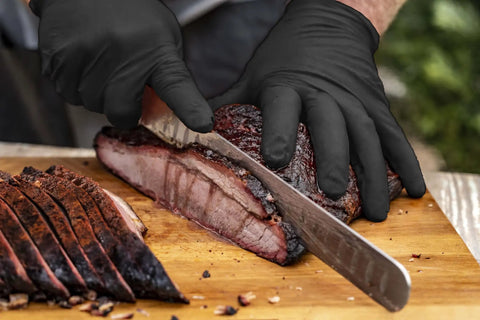 Person slicing meat while wearing Grill Ready Disposable BBQ Gloves Kit With 50 Nitrile Gloves, Powder Free, Latex Free, Food Safe.