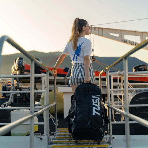 Person on dock with Roller Mesh Dive Gear Bag With Large Outer Pocket And Internal Pocket, Adjustable Shoulder Strap, Top And Side Handles