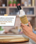 Hand holding 12 oz bottle of Food Grade Mineral Oil For Wood Cutting Boards And Butcher Blocks in kitchen