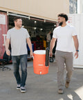 10 Gallon Portable Sports Cooler And Beverage Dispenser with Flat Seat Lid being carried outdoors by two people.