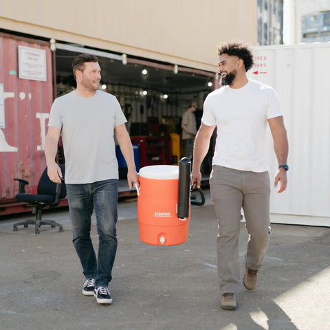 10 Gallon Portable Sports Cooler And Beverage Dispenser with Flat Seat Lid being carried outdoors by two people.