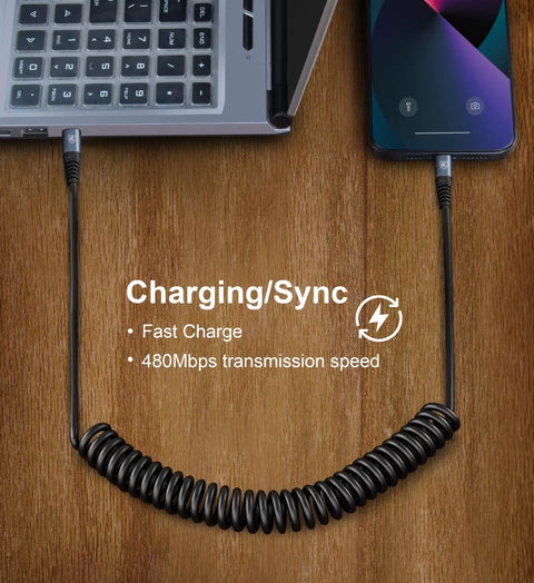 Coiled USB C to Lightning Cable 3Ft 2 Pack for Car Fast Charging connecting laptop and iPhone, wooden desk surface.