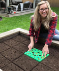 Person using Color Coded Square Foot Garden Spacing Template With Dibber Seed Spoon Ruler And Planting Guide in raised bed.
