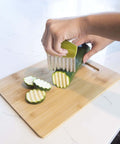 Joie crinkle cutter knife with green handle slicing zucchini on a wooden cutting board; stainless steel blade