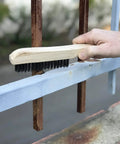 Tough As Nails Welding Chipping Hammer With Comfort Grip Spiral Handle And Anti Rust Tempered Steel Head Plus Stainless Steel Wire Scrubbing Brushes For Mig TIG Cleanup Kit being used to scrub rust off a blue metal fence.