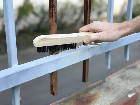 Tough As Nails Welding Chipping Hammer With Comfort Grip Spiral Handle And Anti Rust Tempered Steel Head Plus Stainless Steel Wire Scrubbing Brushes For Mig TIG Cleanup Kit being used to scrub rust off a blue metal fence.