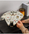 Person assembling Millennium Falcon 3D Model Kit For Star Wars Fans And Collectors, Epic Desk Decor, on bookshelf.