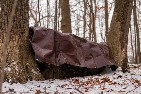 Beastly Heavy Duty 18x24 Foot 16 Mil Poly Tarp covering logs in snowy forest with rust proof grommets for all weather shelter