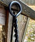 Close-up of 40 Inch Fire Poker For Fire Pit With Twisted Rope Handle in black steel against wood background