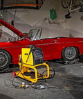 HEAVY DUTY YELLOW POWDER COATED STEEL WELDING CART WITH SMOOTH ROLLING CASTERS AND SLANTED WORK SURFACE BUILT TO CRUSH THE GRIND AND HAUL YOUR GEAR FAST in a garage beside a red convertible car.