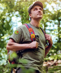 Man wearing 'I Love Camp' pins in forest scene, part of the 'I Love Camp Pins For Kids 60 Pcs Outdoor Camping Button Accessories' set.