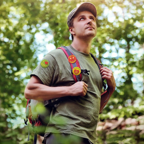Man wearing 'I Love Camp' pins in forest scene, part of the 'I Love Camp Pins For Kids 60 Pcs Outdoor Camping Button Accessories' set.
