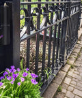 Gate hinge mounted on black ornate iron fence beside a stone walkway